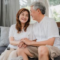 Asian senior couple relax at home. Asian Senior Chinese grandparents, husband and wife happy smile hug talking together while lying on sofa in living room at home concept.